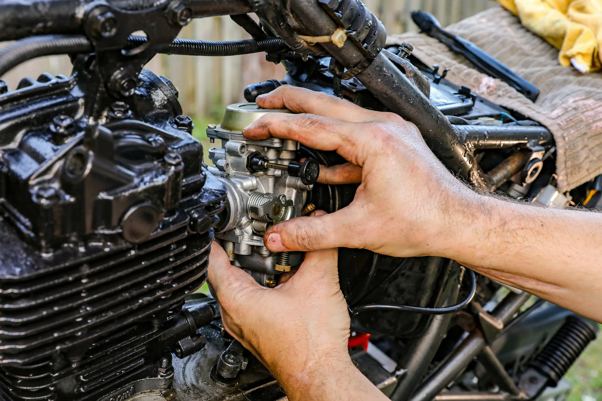 Mains d’un mécanicien sur le carburateur d’une moto